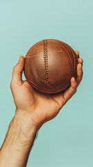 A hand holding a handball with a focus on the grip and seams of the ball, set against a light solid color background