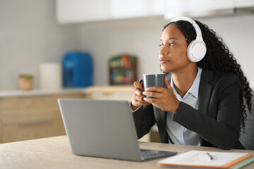 Serious black businesswoman drinking and listening audio