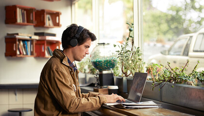 Learning, headphones and man in cafe on laptop for course, college research or music streaming platform. Male student, coffee shop or typing on technology with online network, connection or study app