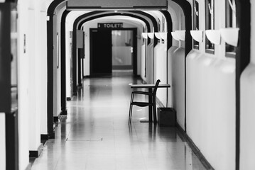 A black-and-white photograph of a long, empty hallway with arched ceilings, featuring a single...