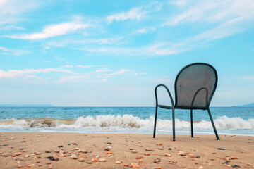 Empty metallic chair on sandy beach in Vrasna Greece. Aegean sea waves splashing the sand shoreline of Strymonic Gulf.