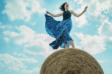 Carefree mature woman wearing skirt standing on hay bale under cloudy sky