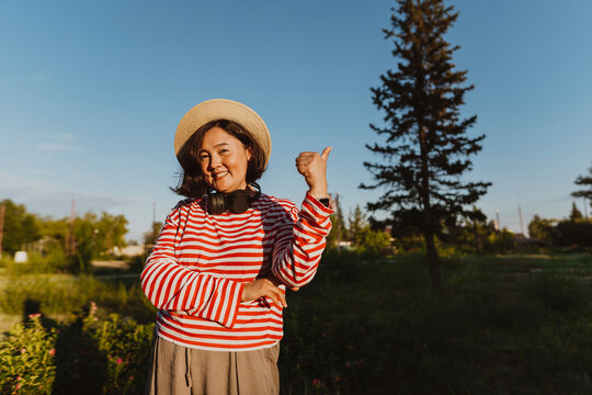 Smiling plus size woman with hat doing thumbs up in sunlight