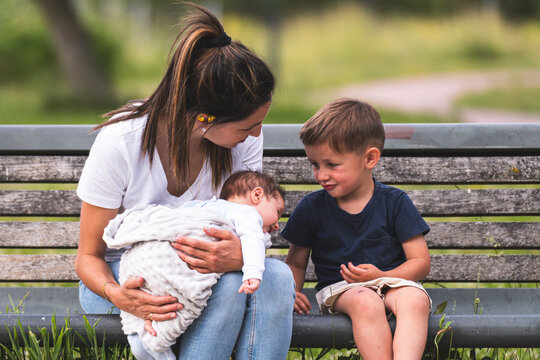 Mother spending leisure time with kids and sitting on bench at playground
