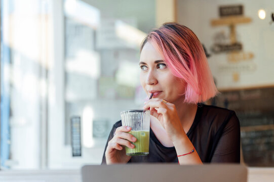 Thoughtful woman with pink hair drinking macha tea at cafe