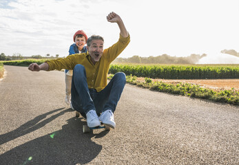 Boy pushing cheerful grandfather on skateboard on road