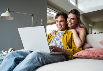 Happy woman leaning on boyfriend using laptop on sofa at home