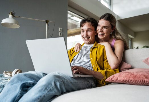 Happy woman leaning on boyfriend using laptop on sofa at home