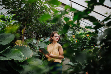 Small greenhouse business. Businesswoman selling flowers and houseplants, holding tablet and smiling.