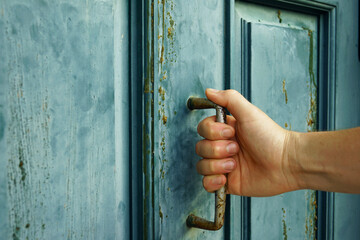 A close-up of a man's hand, fingers wrapped around a handle on a turquoise wooden door. The...