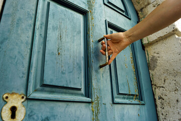 Male hand holding door handle on blue wooden door with unusual keyhole, close-up photo. Entrance to fairy tale: beautiful old door that man is about to open.