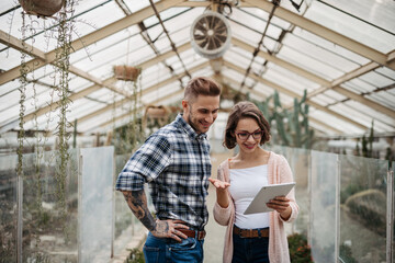 Fototapeta premium Small greenhouse business. Businesswoman and manager talking, standing in greenhouse, looking at camera, smiling.