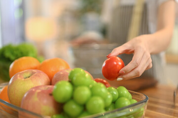 Close up shot of woman picking up fresh tomato in tomato in a bowl on countertop