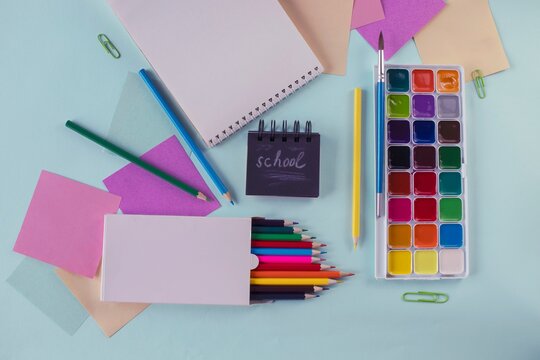 Colored pencils, paints and writing paper in pastel colors, back to school concept, stationery. Flat lay, top view.