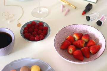 Plate of pastel macarons, cookies and chocolate, cup of tea of coffee, glass of bubble water, various berries, books and accessories on the table. Selective focus, pastel colors.