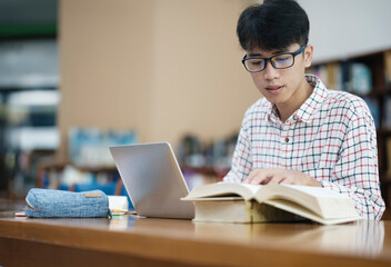 Young Asian male sitting inside a library alone doing research. Man working on a project. Young man doing research for a case.