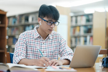 Young Asian male sitting inside a library alone doing research. Man working on a project. Young man doing research for a case.