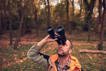 Man using binoculars and camera for bird and animal watching in nature.