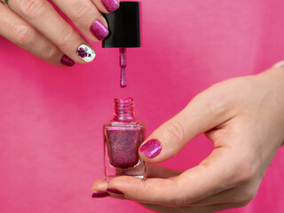 Female hands with pink manicure has pink purple nail polish bottle. Woman holding pink holographic...