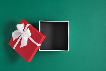 Open red square gift box, present with white satin ribbon with bow on green background. Christmas....