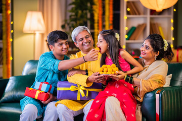 Indian family enjoying Diwali festival night with sweets and gifts in traditional attire at home
