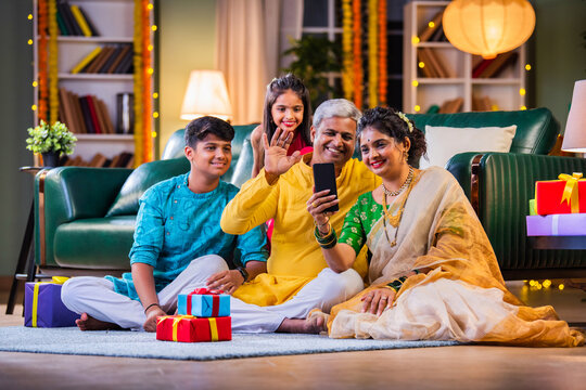 Indian family in festive attire making a video call during Diwali, surrounded by gifts on the sofa