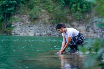 Fototapeta premium a young woman squats by the shore of the lake and enjoys the refreshing coolness and beauty of the lake