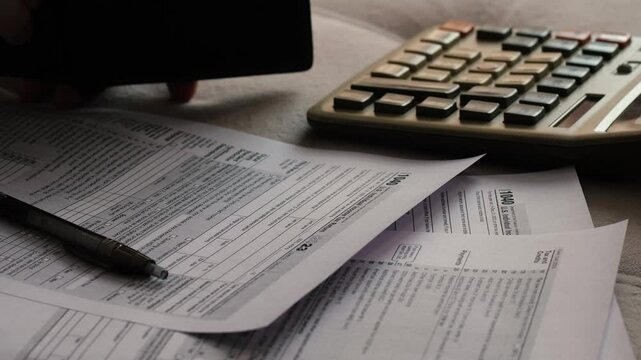 topic of payment and calculation of taxes by US citizens, male hand holding wallet counting on calculator and filling out tax form 1040