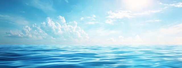 Fototapeta premium A vast expanse of water beneath a clear blue sky Sunlight gleams atop the surface, while clouds scatter above