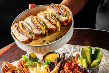 A close-up of a gourmet sandwich cut in half, showcasing layers of meat, cheese, lettuce, and tomato. Served on a plate with crispy fries and garnish. Perfect for food photography