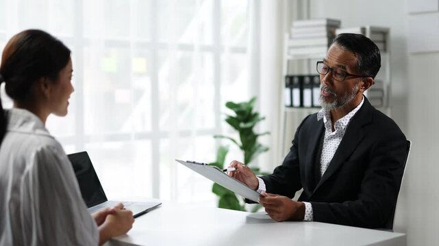 Interviewer evaluating candidate in formal setting. Professional recruiter interviewing a candidate in office, asking questions, reviewing documents, discussing qualifications, and evaluating skills.