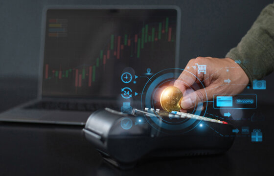 A hand holding a Bitcoin coin over a payment terminal, symbolizing cryptocurrency transactions, with a stock market graph in the background.