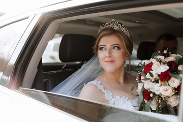 A bride is sitting in a car with a bouquet of flowers in her lap. She is wearing a tiara and a veil