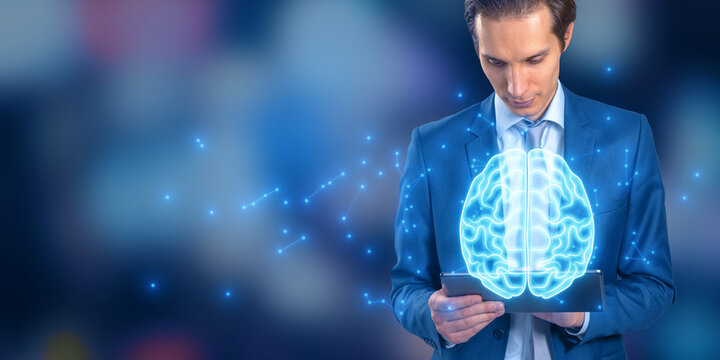 Attractive young european businessman using tablet using glowing polygonal brain hologram on blurry bokeh background. Artificial intelligence and machine learning concept.