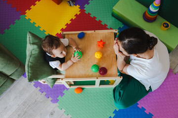 Concentrated boy during SIT classes with educational psychologist holding colored ball for...