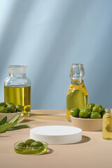 Pedestal for display cosmetic product of olive extract with white empty podium, fresh olives and olive oil on blue background. Olives contain many healthy nutrients