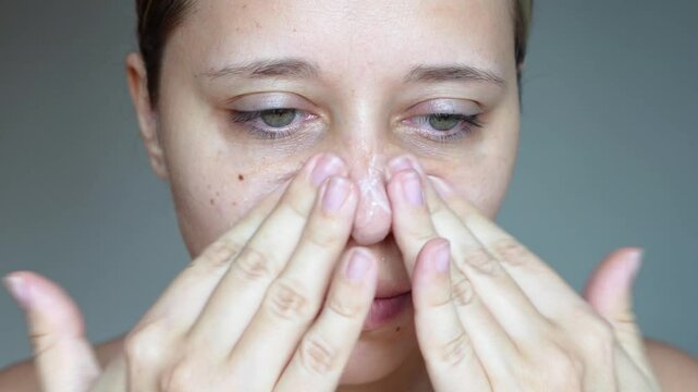 Young caucasian woman cleansing the face with scrub massaging skin of nose and cheeks on dark grey background. Skin care. Washing with a scrub, peeling, getting rid of pores from black dots. Close up