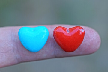 Obraz premium two small red blue plastic hearts toy lie on a finger of a hand on the street