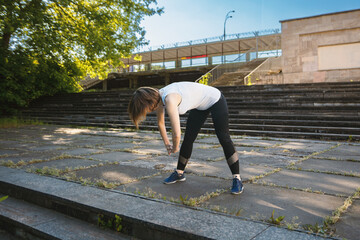 An adult woman is doing fitness in the park. The woman is bending forward.