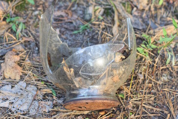 one large gray broken glass jar with a hole closed brown rusty metal lid lies on the ground in...