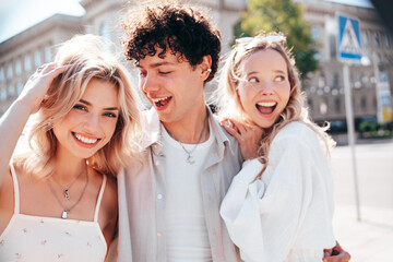 Young three stylish friends posing in the street. Fashion man and two cute female dressed in casual summer clothes. Smiling models having fun. Cheerful women and guy outdoors, in sunny day