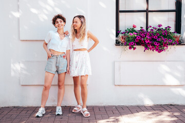 Two young beautiful smiling cute women in trendy summer sundress. Sexy carefree models posing in the street in sunny day. Positive models having fun and hugging. Cheerful and happy, Europe, Santorini