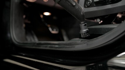 Car detailer cleaning the interior of a car door using a small vacuum cleaner with a brush head.