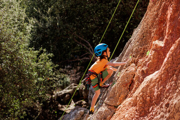 child is rock climbing at a summer camp. rock climber boy. sport in nature. cute teenager climbs a rock with a belay. active holidays.