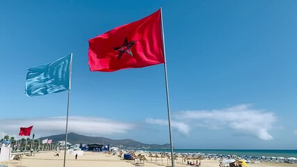 Slow-motion footage of the Moroccan red flag waving around outdoors with a blue sky and the north beach in the background
