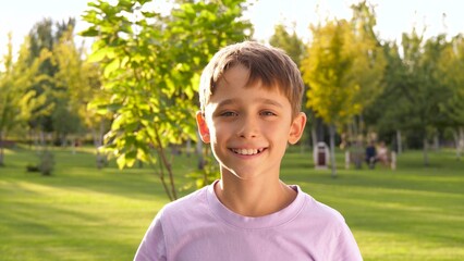 The face of a happy boy in the background of a park. the face of a smiling child in the sunlight on...