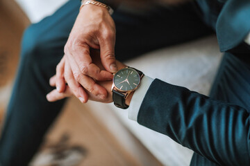 A man is wearing a watch and is looking at it. He is wearing a suit and tie