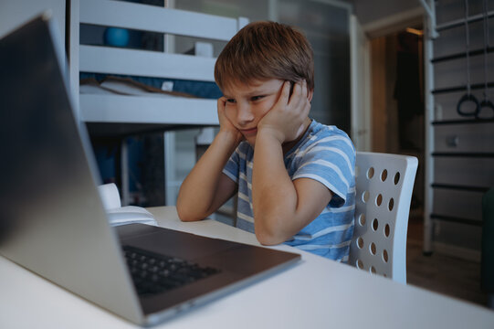 cute little boy studying at home usung laptop, tired, sressed, thinking hard trying to do homework