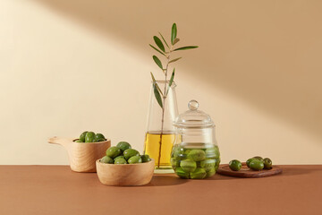 Fresh olives decorative on wooden bowls and a glass vase containing olive oil on a beige background. Minimalist scene for advertising, olive material with many uses