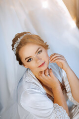 A woman is wearing a white robe and a tiara. She is looking at the camera with a smile on her face